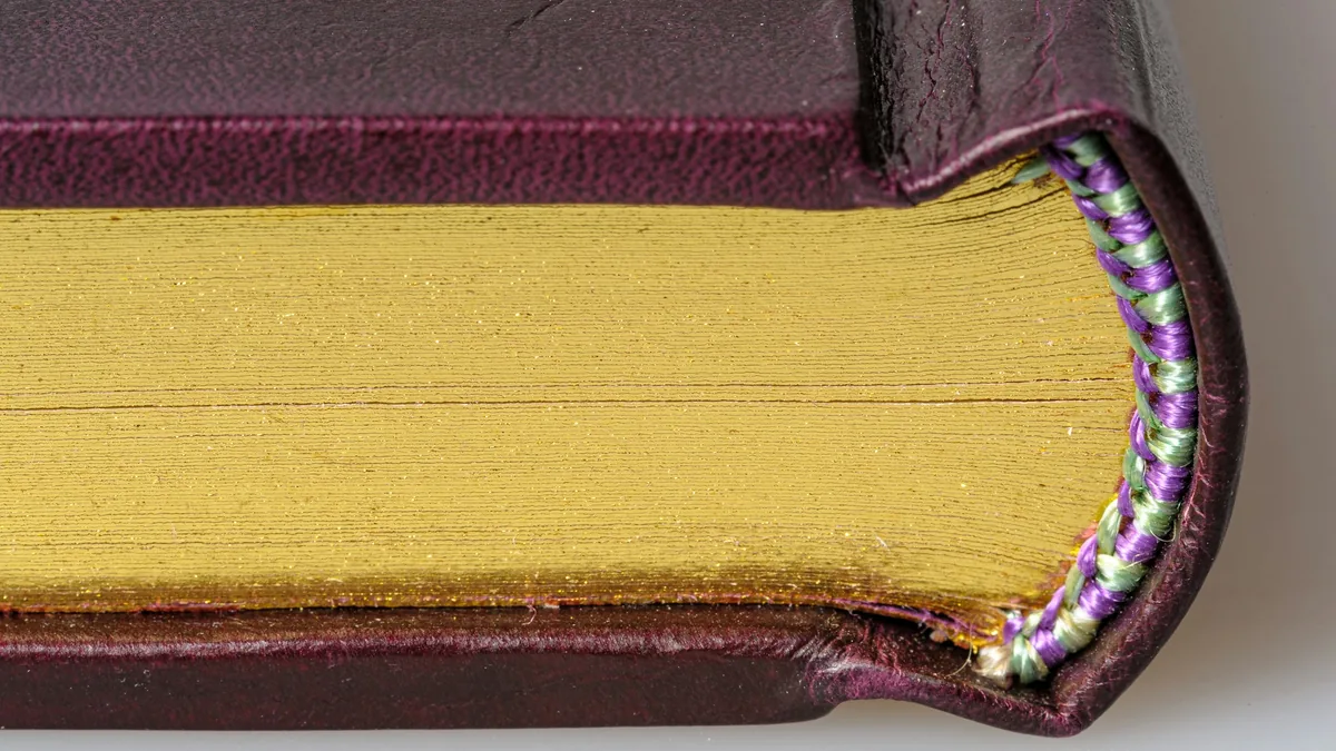 Esquina de un libro encuadernado en piel con cortes dorados y cabezada cosida a mano en hilo verde y morado